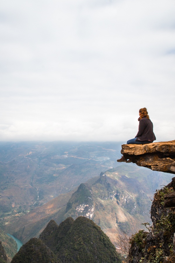 Une femme seule surplombant le paysage au Vietnam alors qu'elle est assise sur un rocher.