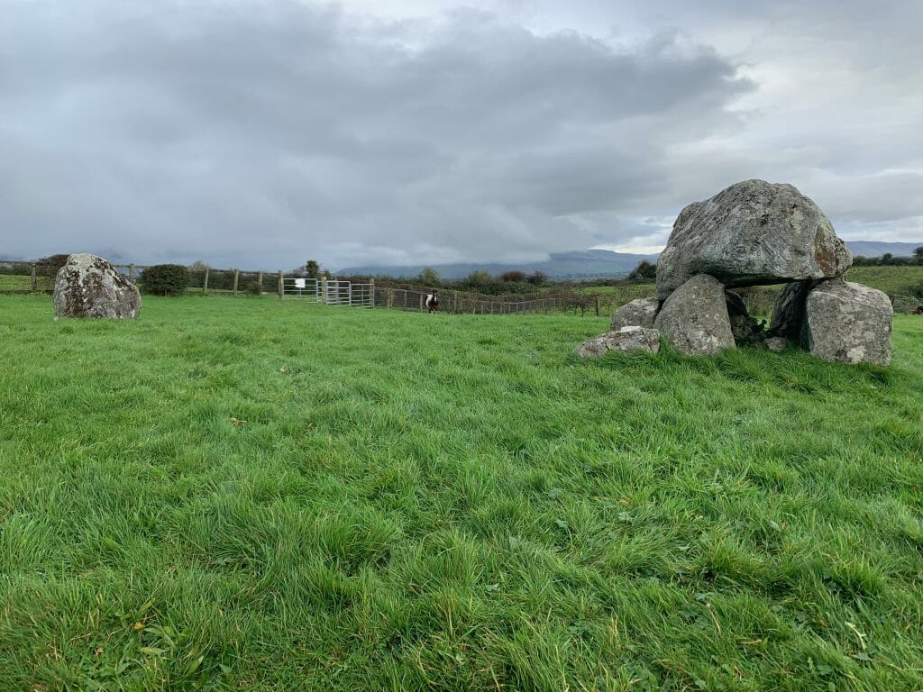 Pâturages verdoyants avec structures en pierre néolithiques à droite et à gauche de l'image, ciel gris