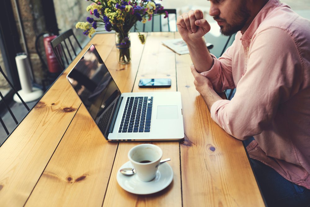 Homme indépendant qui se connecte au WiFi via un ordinateur portable, un homme d'affaires réfléchissant qui travaille sur un ordinateur portable pendant qu'il est assis sur une table en bois à l'intérieur moderne d'une cafétéria, un étudiant qui lit du texte ou un livre dans une cafétéria