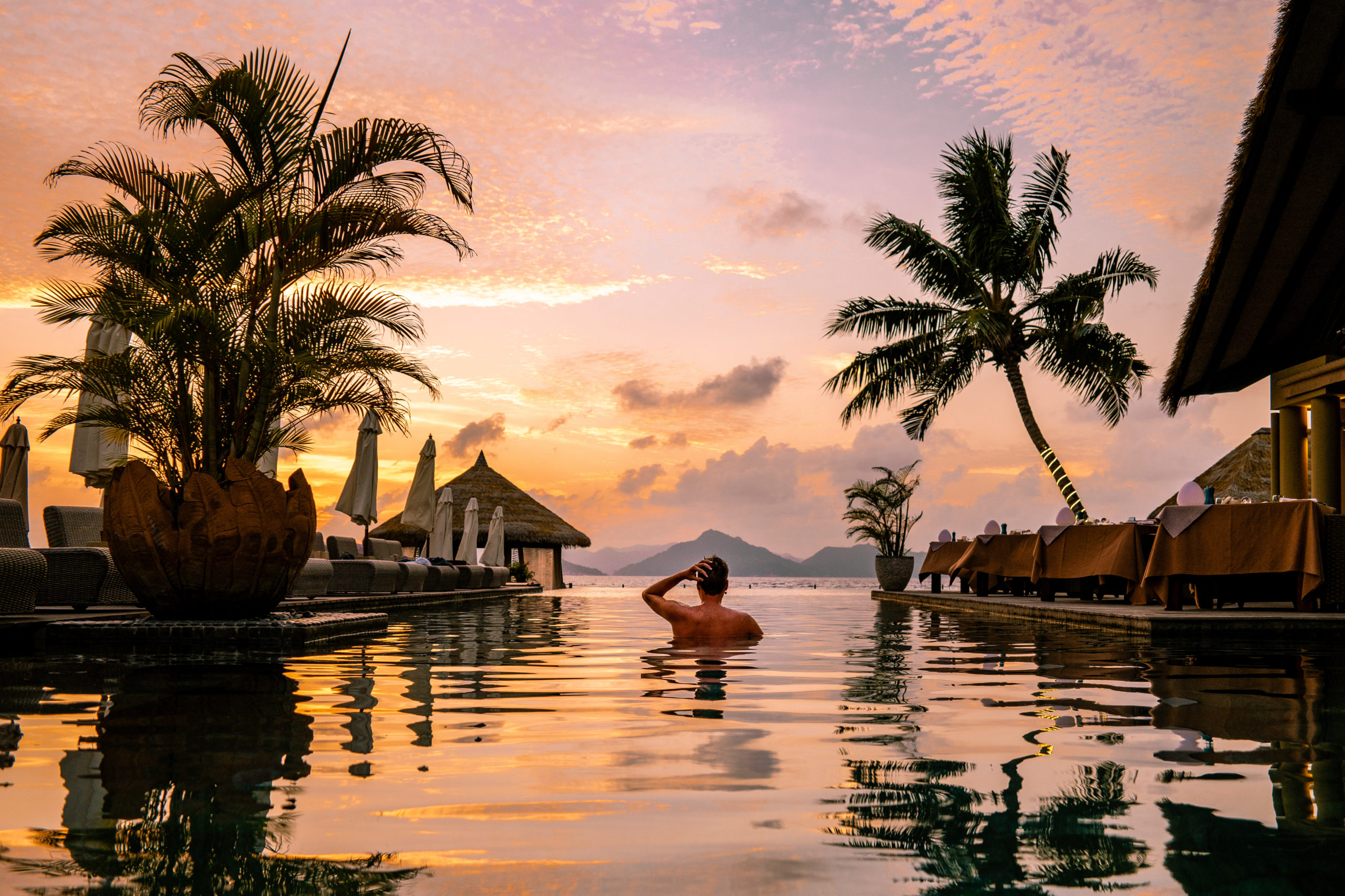 Coucher de soleil aux Seychelles, homme nageant dans la piscine du complexe