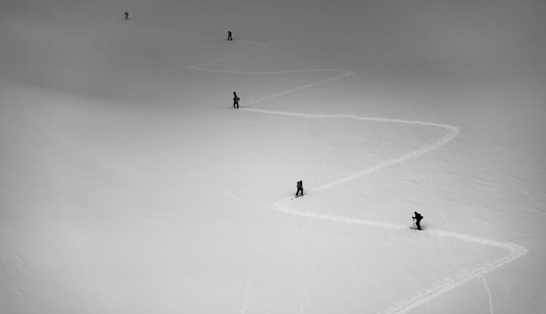 Una montaña con 5 esquiadores de fondo subiendo por el camino que ha trazo el primero