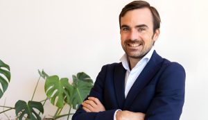 Posado corporativo de Nacho Navarro en traje y con los brazos cruzados al lado de una planta