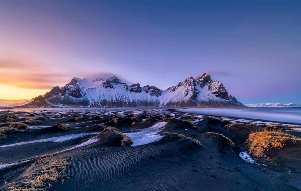 Montagnes pointues de Vestra Point sous la neige et le ciel violet.