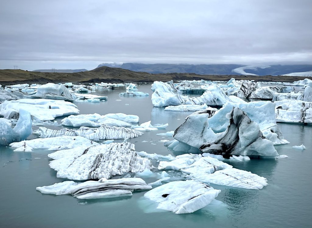 Un lagon encore gris rempli de morceaux de glace flottante.